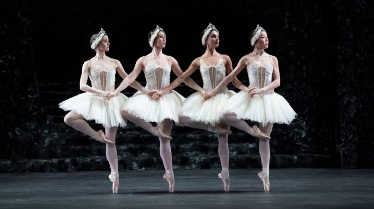 Line of dancers en pointe holding hands in white tutus