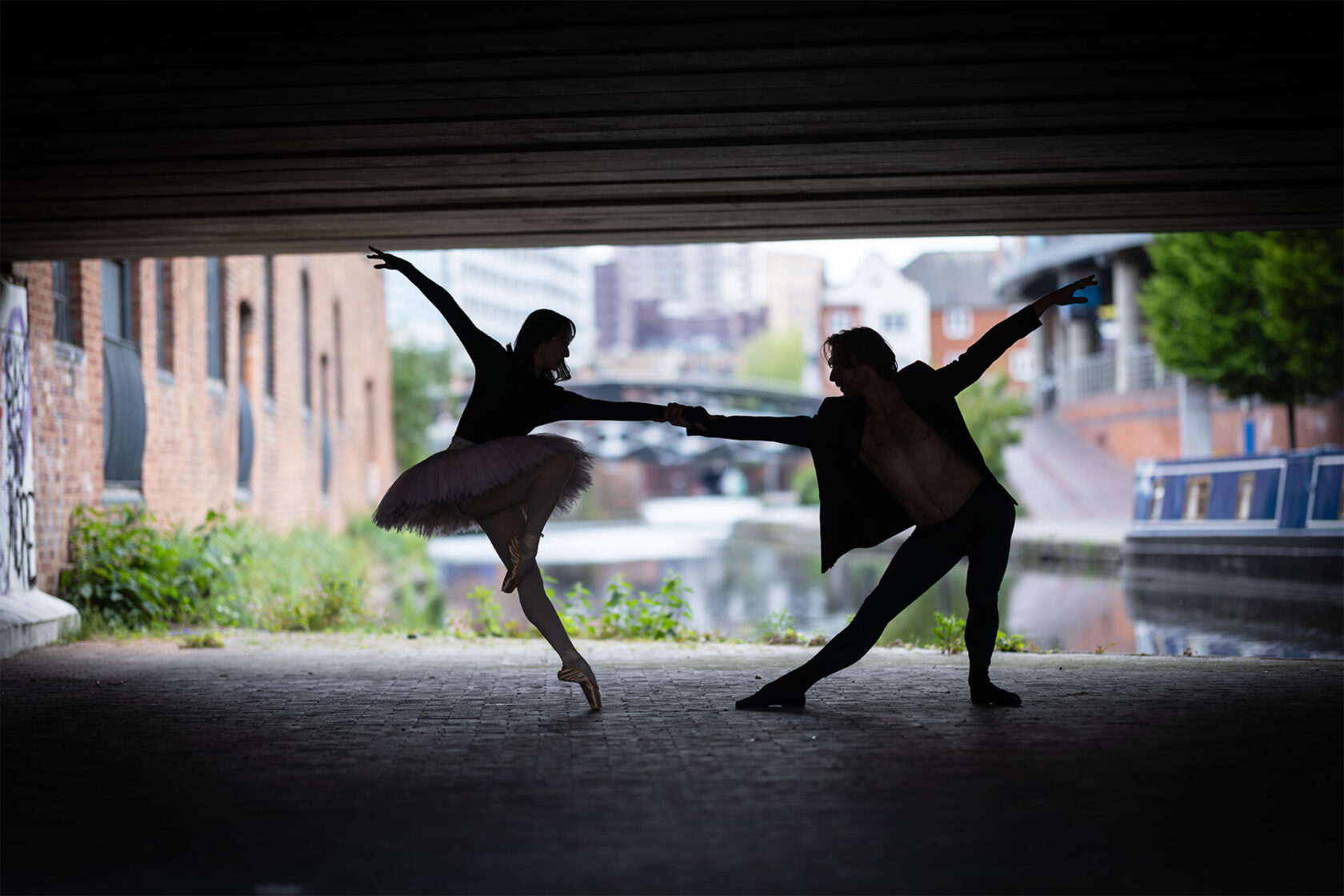 male and female dancers in silhouette under a bridge