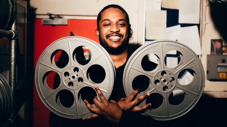 smiling man holds large film reels