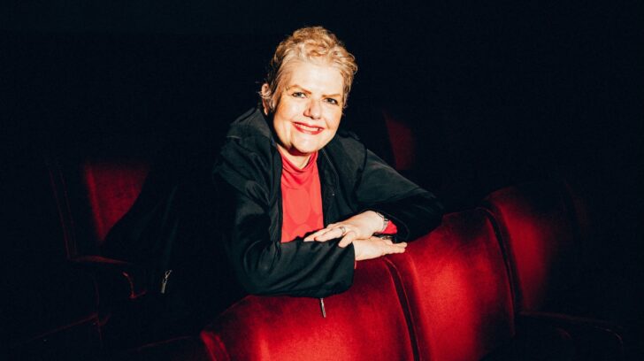 person leans forward on red cinema chair smiling