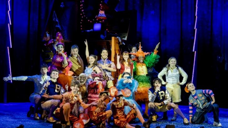 large group of young actors on stage in brightly coloured costumes
