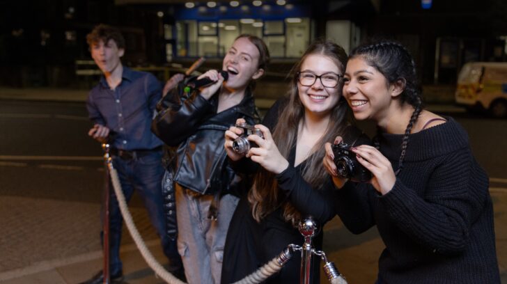 young people taking photos and singing with a microphone outside theatre by red carpet